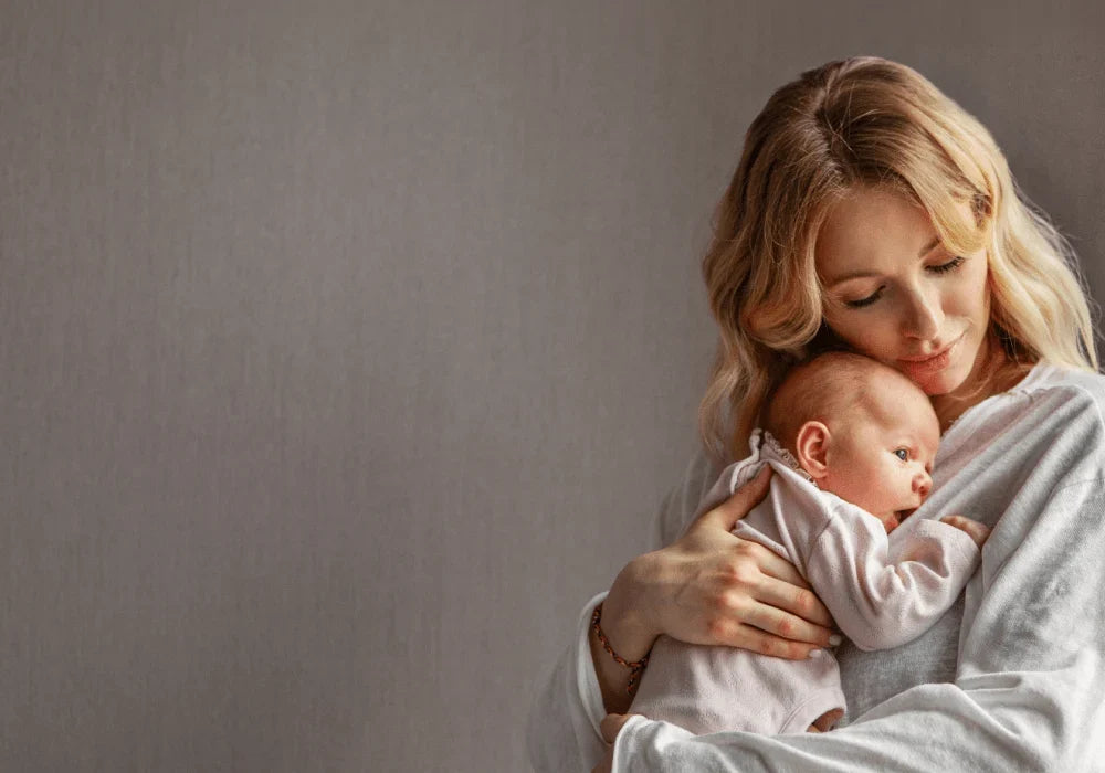 A mother with blonde wavy hair tenderly cradles her newborn baby against her chest, embodying the peace of mind Babysense video baby monitors provide for parents